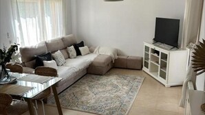 A living room with a sectional sofa, a glass-top dining table, wicker chairs, a patterned rug, a TV on a white cabinet, and two pendant lights. - Baron Villa With Private Heated Pool on Mar Menor (Torre-Pacheco)