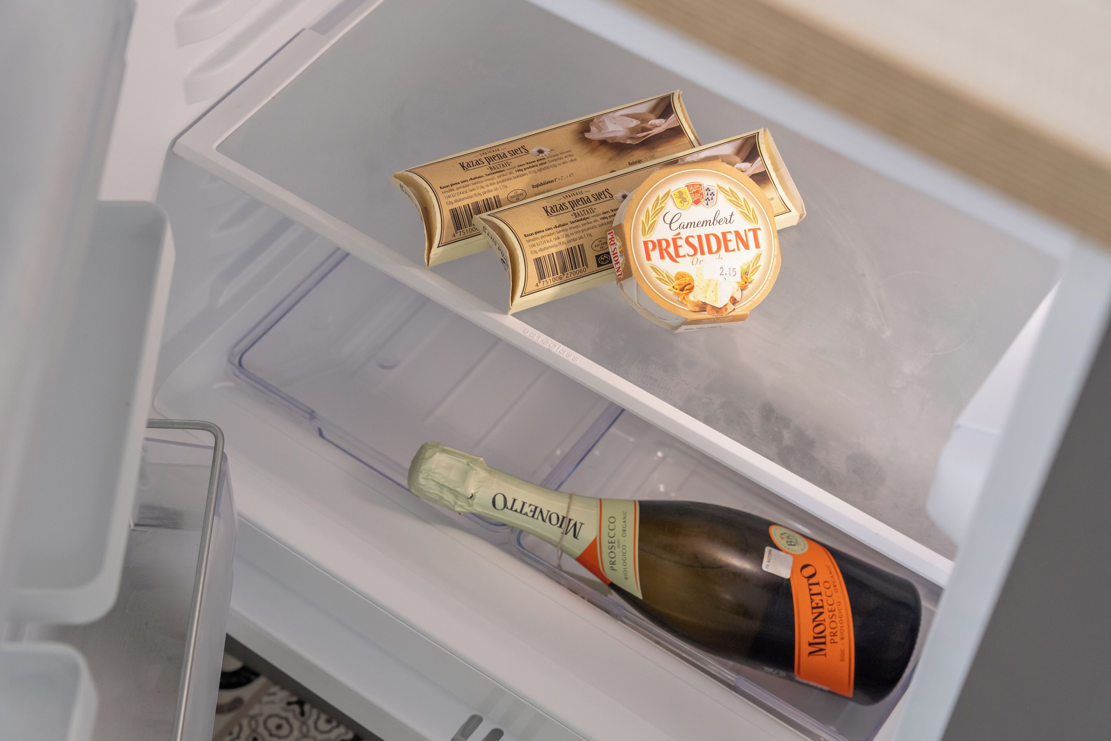 Un frigorifero con una bottiglia di Prosecco Monello e un contenitore di formaggio Camembert President.