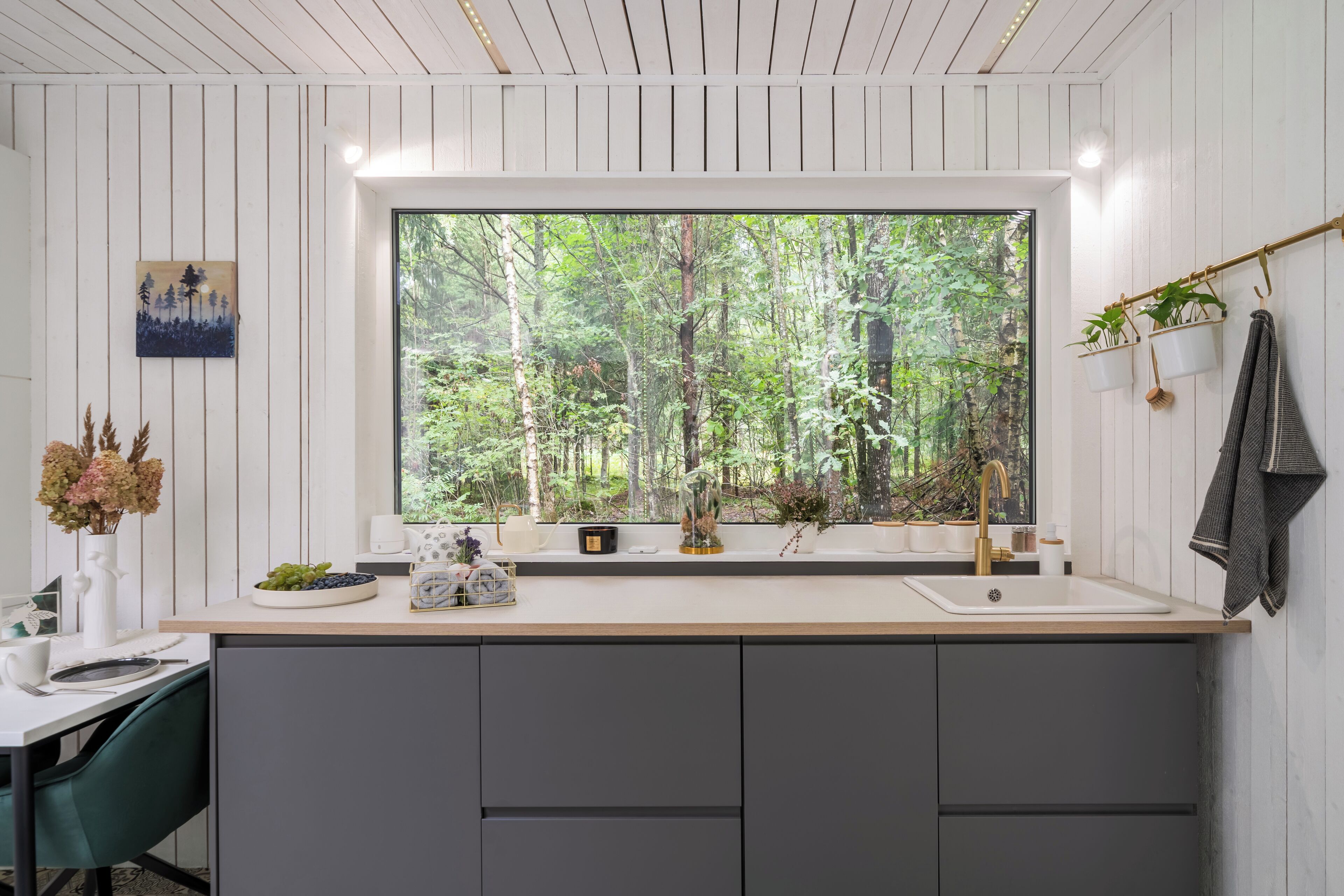 Una cocina moderna con un ventanal grande, un lavamanos y una zona de comedor con una silla verde.