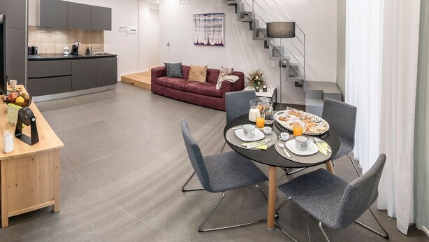 A modern kitchen with grey cabinets, a wooden dining table with chairs, a staircase, and a living area with a sofa and artwork. - Three houses Toledo (Naples)