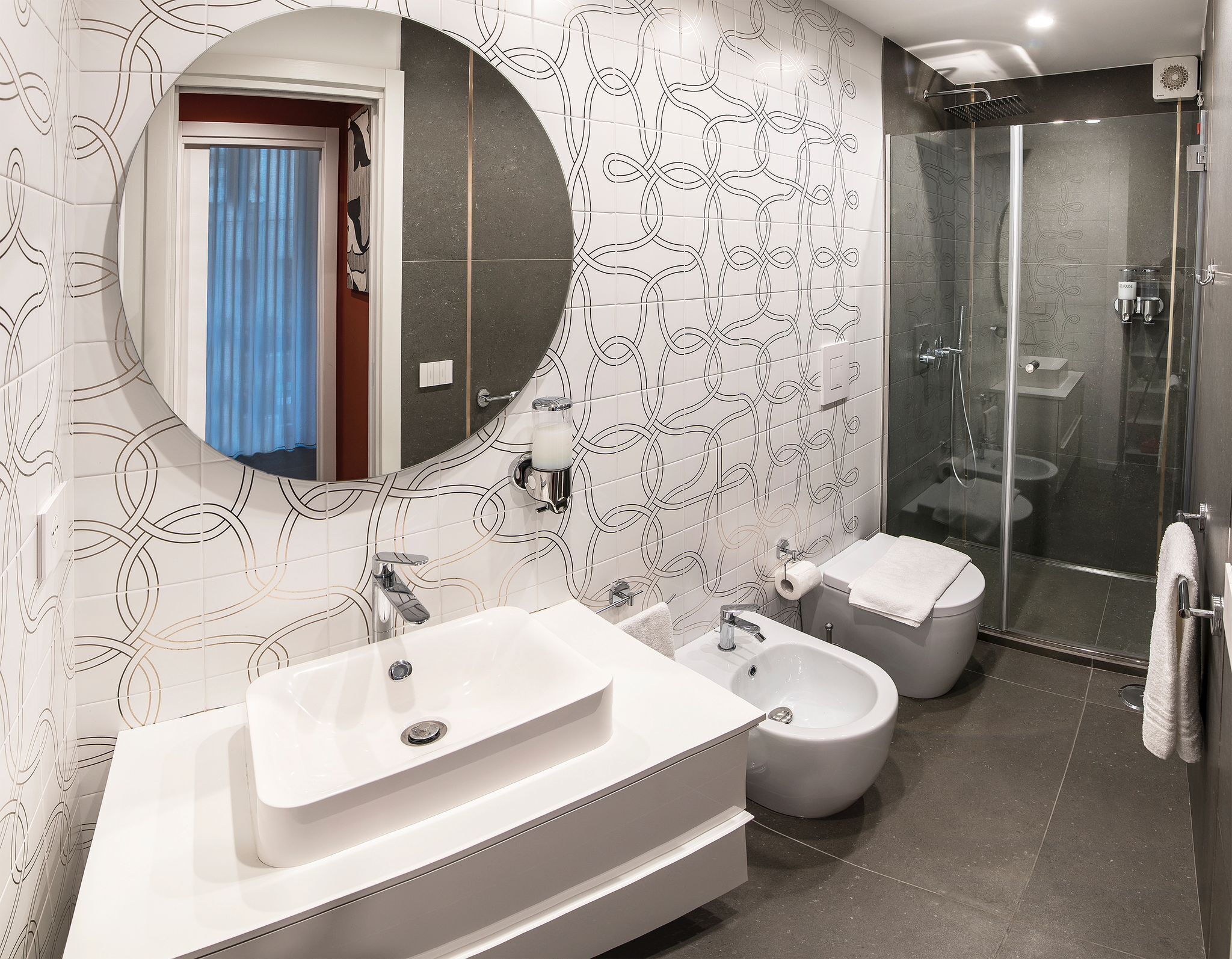 A modern bathroom with a large mirror, two sinks, a bidet, and a glass-enclosed shower.