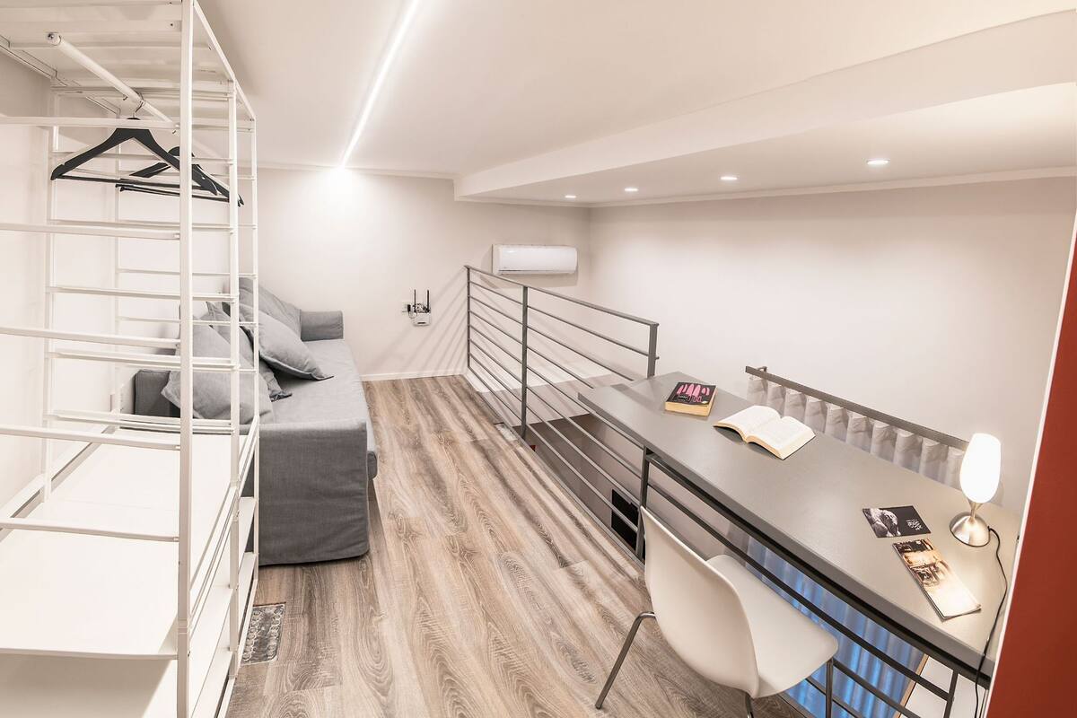 A compact bedroom with a bed, a desk, and a chair. There is a white wardrobe with shelves and a hanging rack.