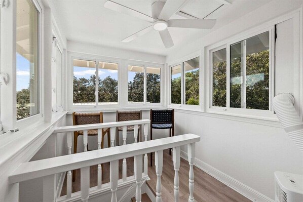 A sunroom with white walls, large windows, and a ceiling fan.