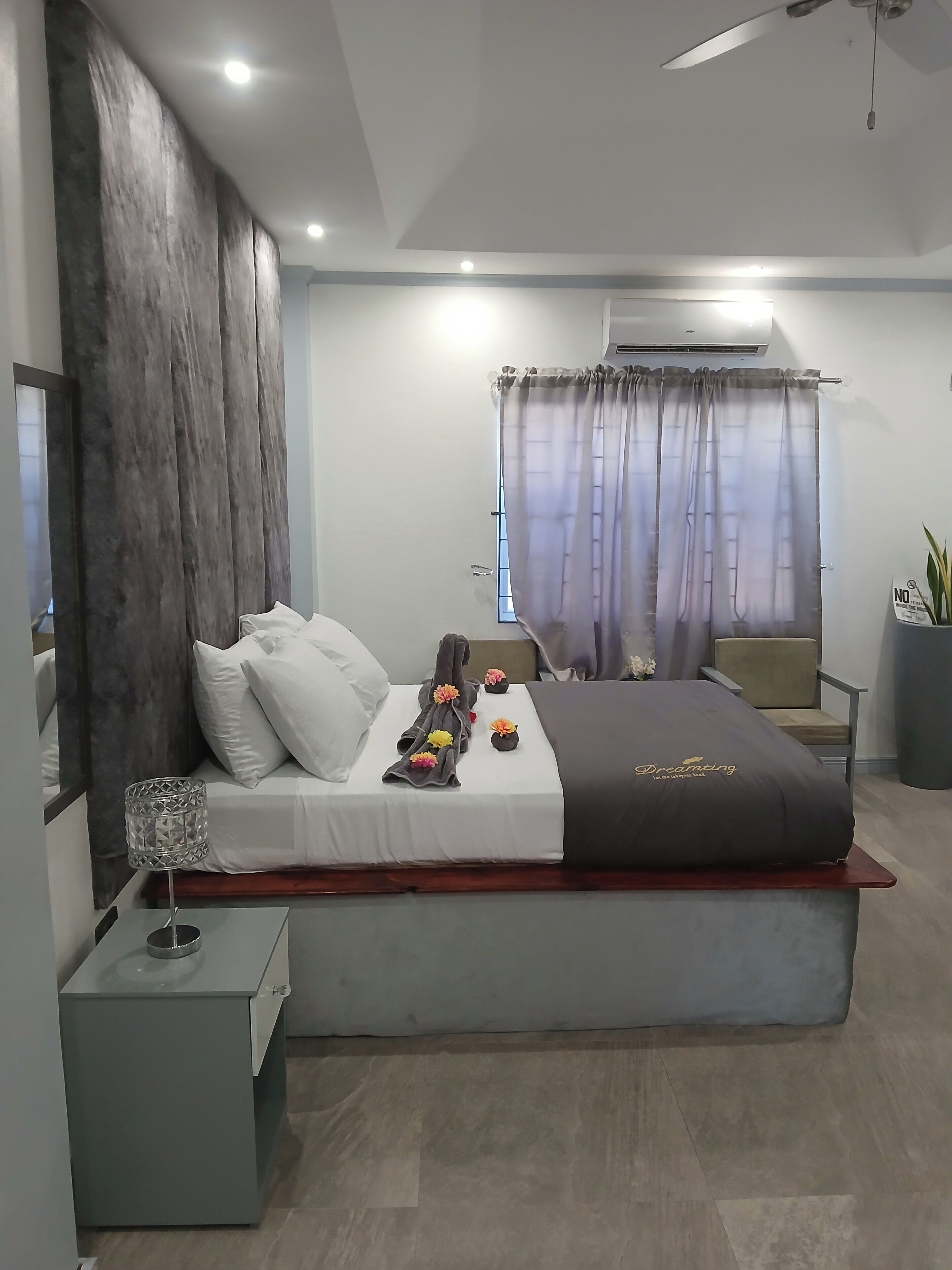 A modern bedroom with a large bed, a bedside table, a chair, and a potted plant.