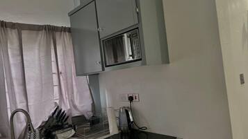 Una cucina con forno a microonde integrato, lavello e piano di lavoro con bollitore e utensili.