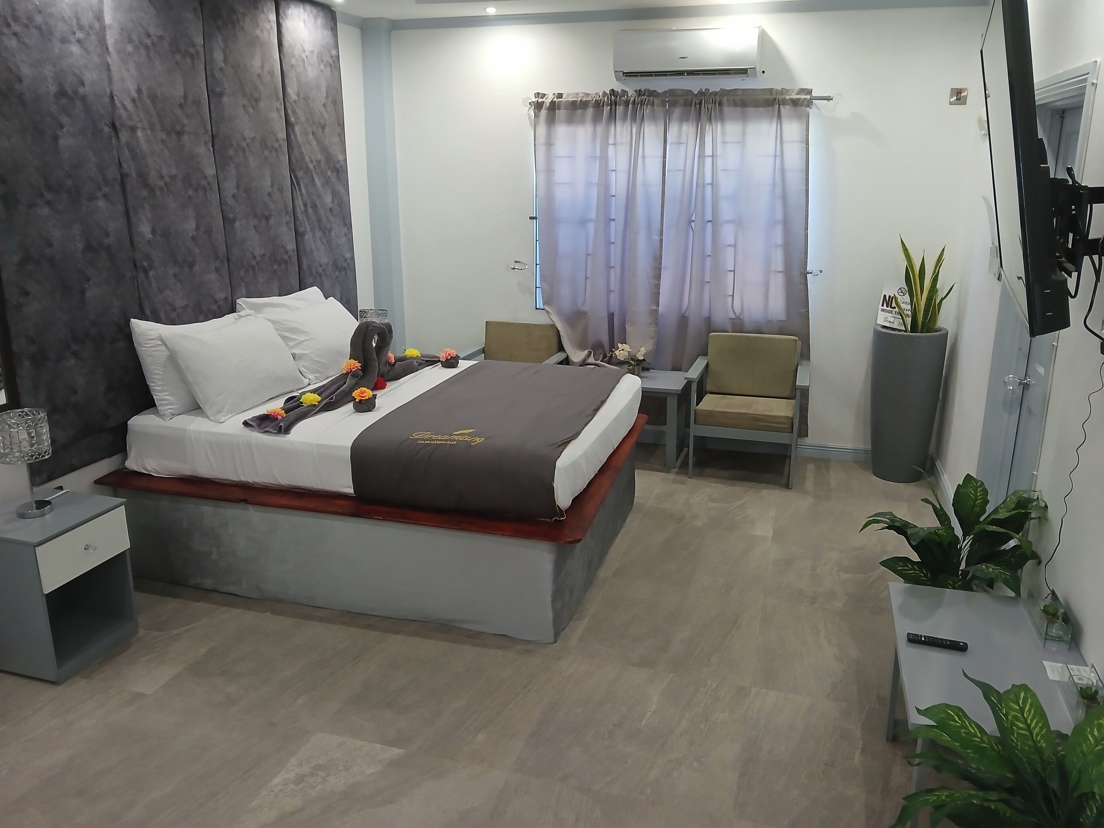 Quarto de hotel moderno com uma cama grande, mesa de cabeceira, uma cadeira, planta em vaso e ar condicionado.
