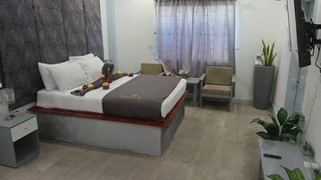 Quarto de hotel moderno com uma cama grande, mesa de cabeceira, uma cadeira, planta em vaso e ar condicionado.