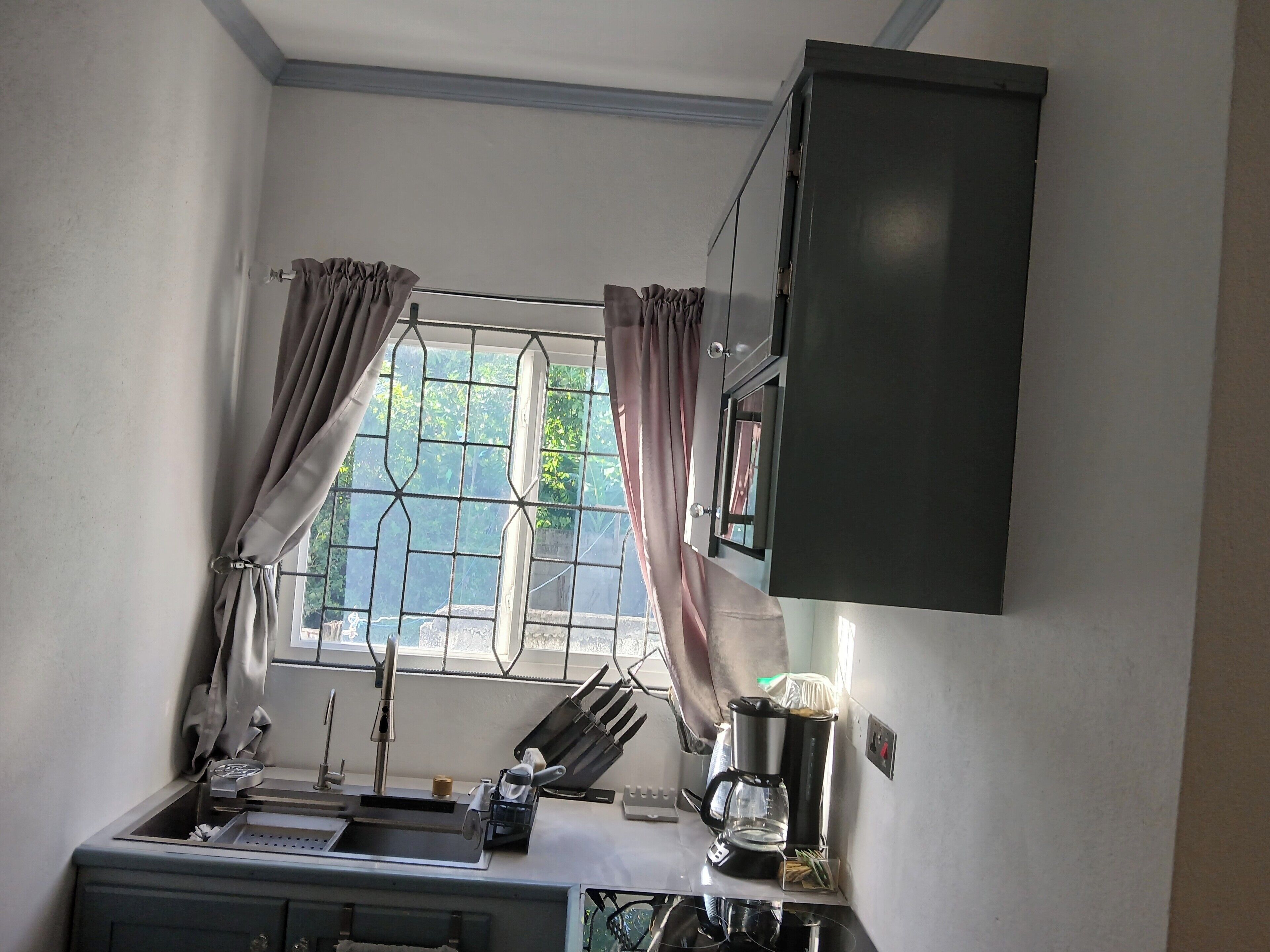 A compact kitchen with a sink, a coffee maker, and a window with curtains.