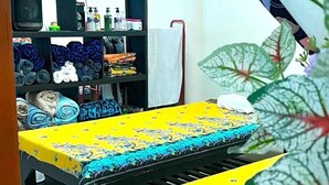 A dining area with a yellow tablecloth, black wooden chairs, and a shelf with folded clothes and toiletries. - Modern Bungalows (Ko Chang)