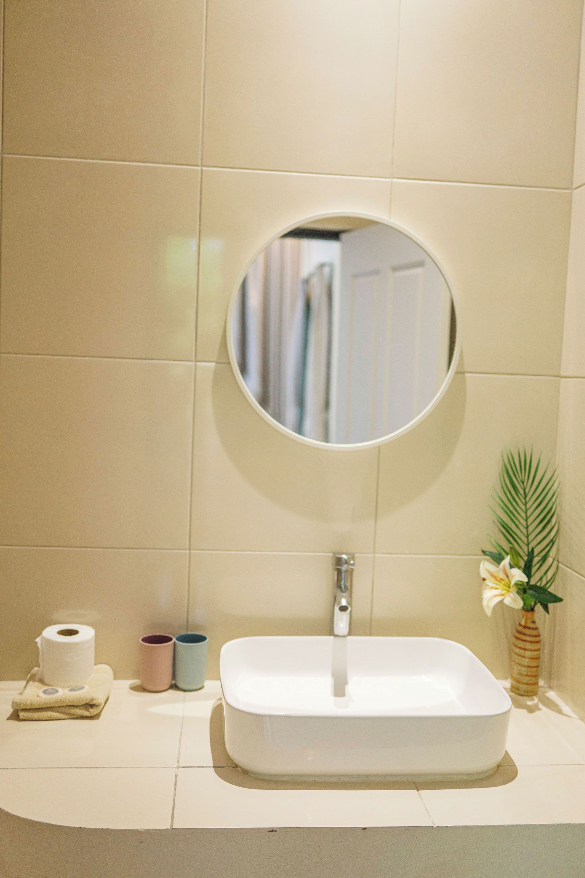 A bathroom with a white sink, a round mirror, and a potted plant.