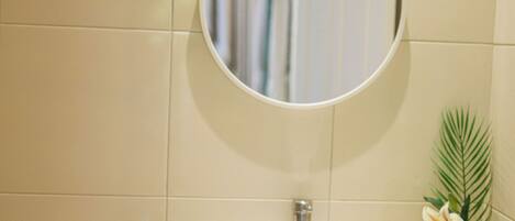 A bathroom with a white sink, a round mirror, and a potted plant.