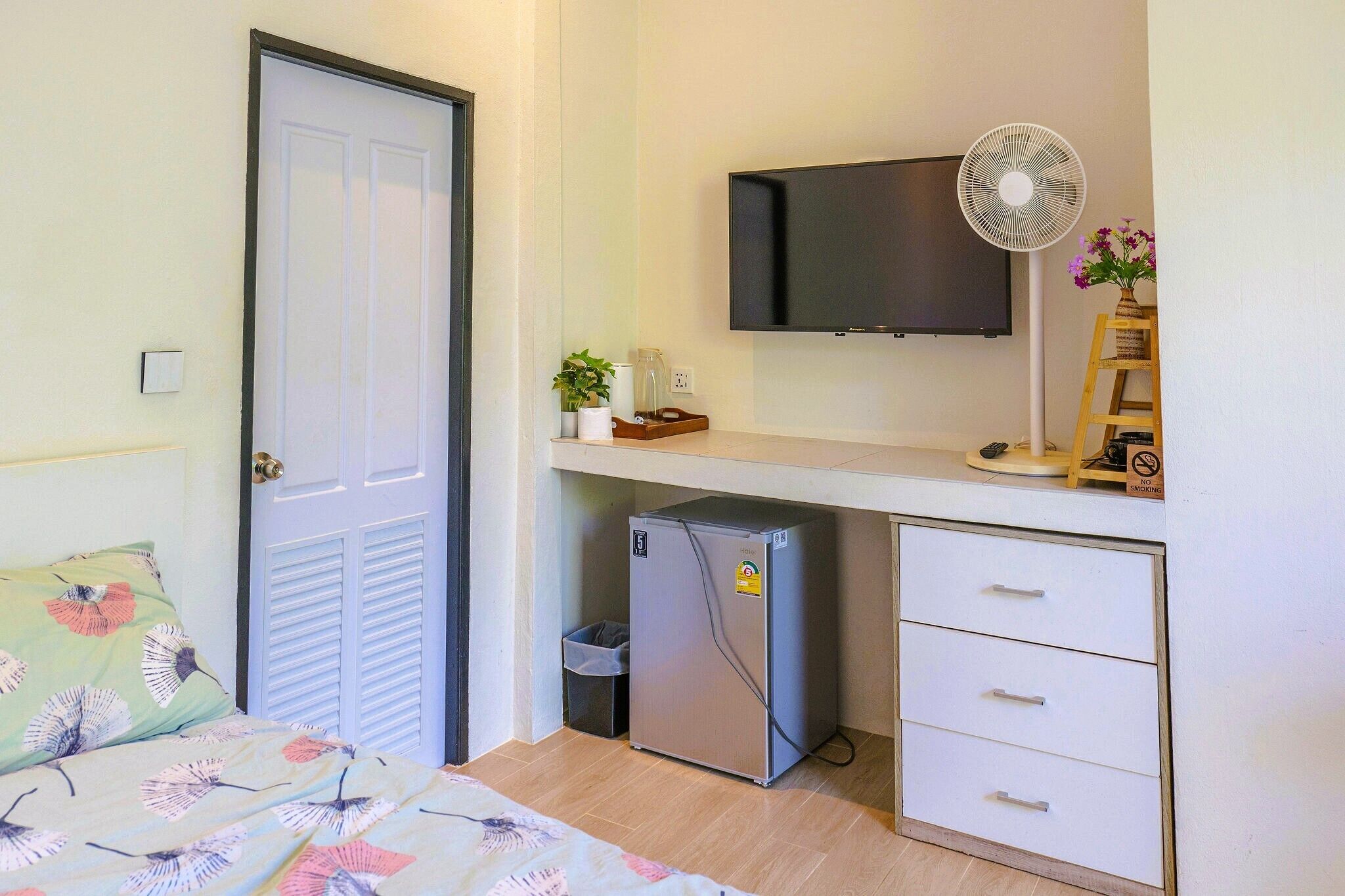 A compact room with a bed, a small refrigerator, a TV, and a desk with drawers.