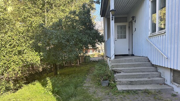 Een huis met een veranda, een kleine tuin en een met baksteen bestrate opgang naar de deur.