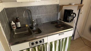 Een kleine keuken met een dubbele spoelbak, een koffiezetapparaat en een klein kastje.