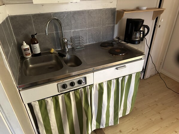 Una cocina compacta con un lavamanos doble, una cafetera y un estante pequeño.