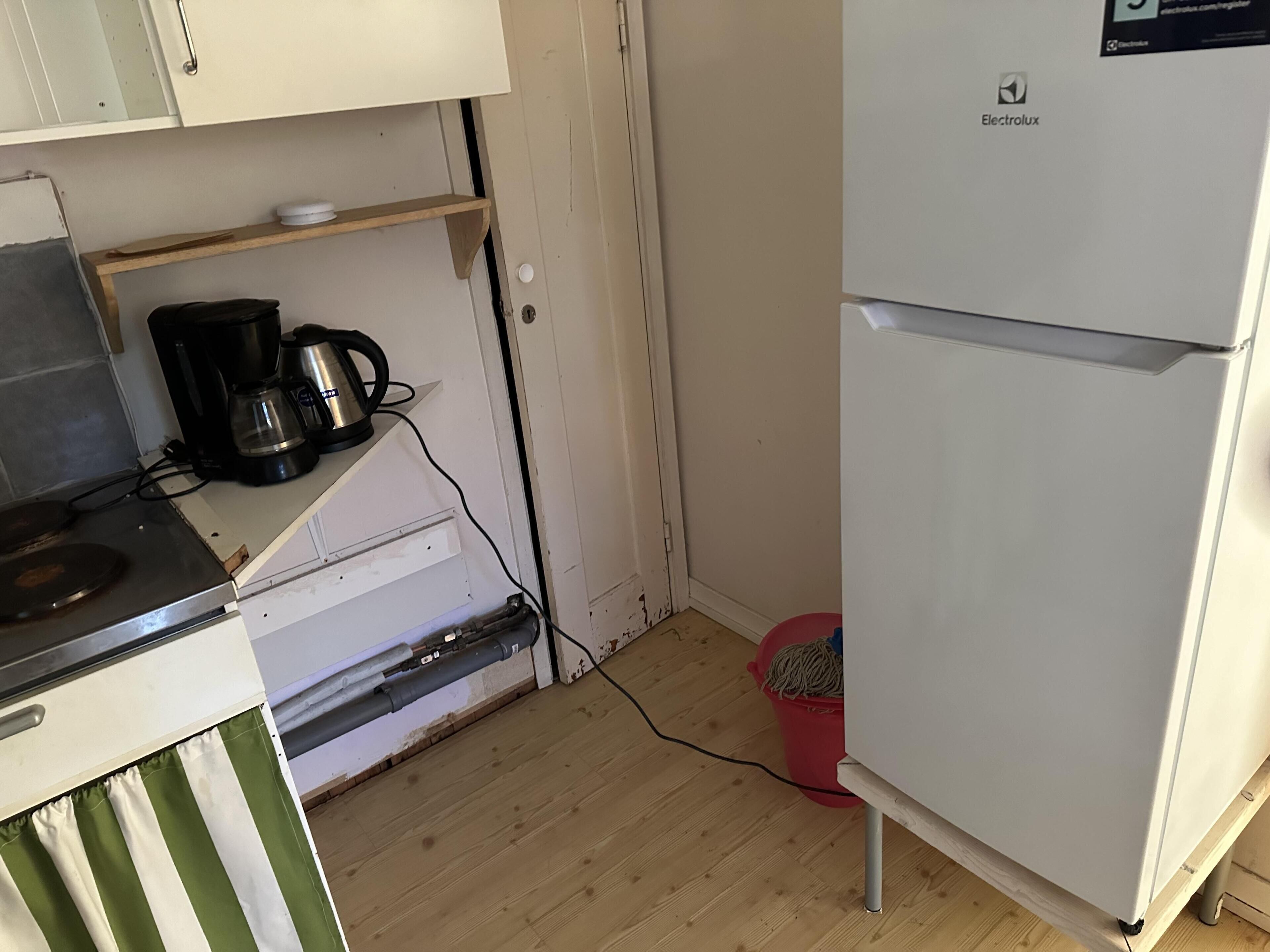 A compact kitchen with a white refrigerator, a coffee maker, and a red trash bin.