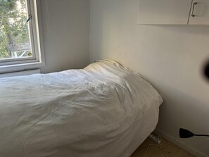 Un dormitori amb un llit, una finestra i una làmpada penjada a la paret.