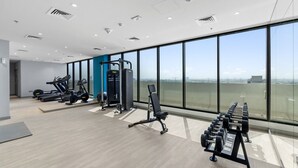 A modern gym with cardio machines, weightlifting equipment, and large windows offering a city view. - Elegant Studio with Pool Access  Private Terrace (Dubai)