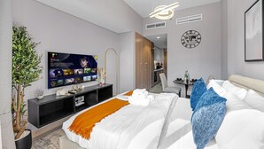 A modern hotel room with a large flat-screen TV, a bed with white and blue bedding, a small table with a vase, and a potted plant. - Elegant Studio with Pool Access  Private Terrace (Dubai)