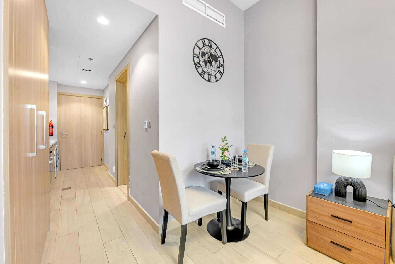 Une chambre d’hôtel moderne dotée d’un coin repas comprenant une table ronde, des chaises et une horloge murale.