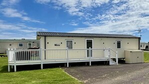 A single-story mobile home with a front porch, a small attached garage, and a clear sky. - Tranquil Seaside Caravan Retreat in Eyemouth (Eyemouth)