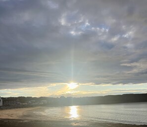 A coastal scene with the sun setting over a body of water, casting a reflection on the surface.