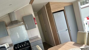 A compact kitchen with a stove, oven, and a small refrigerator. There is a dining area with a table and chairs. - Tranquil Seaside Caravan Retreat in Eyemouth (Eyemouth)