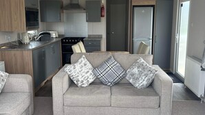 A modern living room with a grey sofa, a wooden coffee table, and a kitchen area with grey cabinets and a stove. - Tranquil Seaside Caravan Retreat in Eyemouth (Eyemouth)