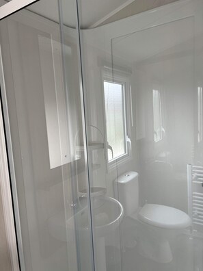 A bathroom with a glass partition, a toilet, a sink, and a window.