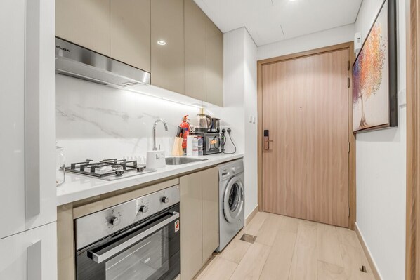 A compact kitchen with a gas stove, oven, microwave, and a washing machine.