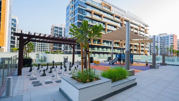 Un espacio exterior moderno con un tablero de ajedrez, asientos y un parque infantil.