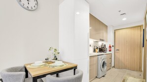 A modern kitchen with a washing machine, a dining area with a table and chairs, and a clock on the wall. - Sleek Studio in Dubai (Dubai)