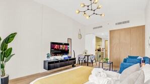 A modern hotel room with a bed, a TV, a dining area, and a kitchen in the background. - Sleek Studio in Dubai (Dubai)