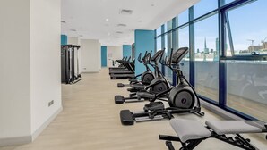 A modern gym with cardio machines, weightlifting equipment, and large windows offering a view of the city skyline. - Sleek Studio in Dubai (Dubai)