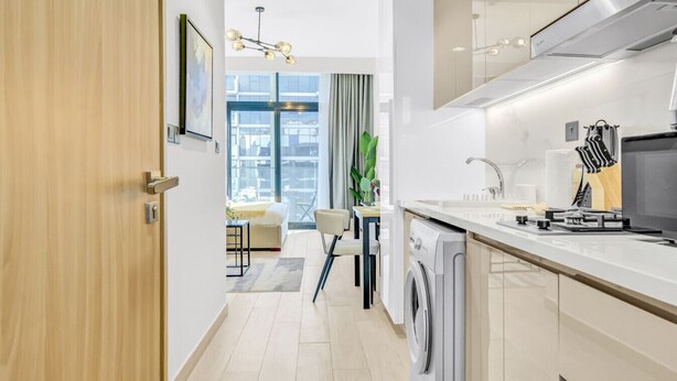 A modern kitchen with a built-in washing machine, a dining area with a view, and a large window. - Sleek Studio in Dubai (Dubai)