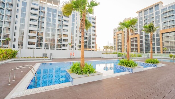 A modern residential building with a rooftop swimming pool, surrounded by palm trees and a clear sky. - Chic Studio Oasis in Dubai (Dubai)