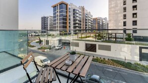 Un balcón con mesa y sillas de madera, con vistas a una zona urbana moderna con edificios altos y una calle con vehículos.