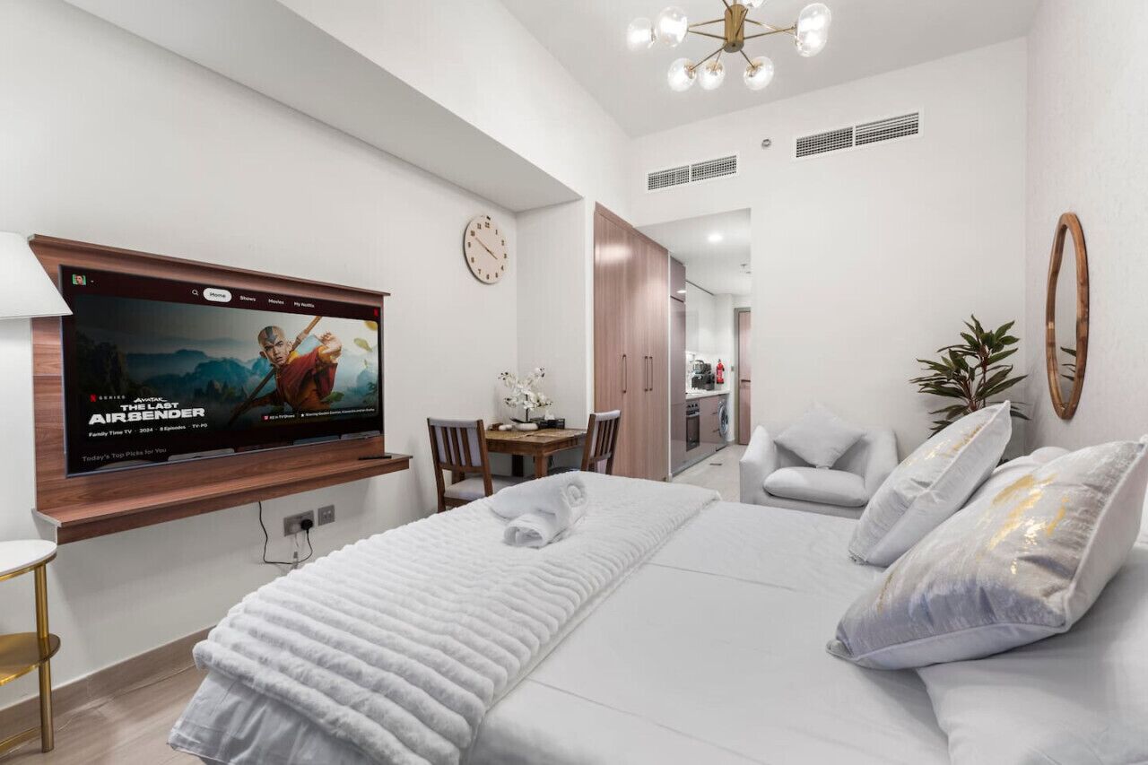 Une chambre d’hôtel moderne avec un grand lit, un téléviseur fixé au mur, un coin repas et une cuisine à l’arrière-plan.