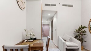 Een eetgedeelte met een houten tafel, stoelen en een vaas witte bloemen. Er hangt een klok aan de muur en staat een plant op de vloer.