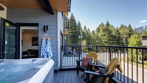 A balcony with a hot tub, a chair, and a table with a blanket. - Cedar and Loam by Revelstoke Vacations (Revelstoke)