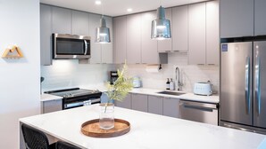 A modern kitchen with stainless steel appliances, a white marble countertop, and pendant lighting. - Cedar and Loam by Revelstoke Vacations (Revelstoke)