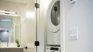 A modern laundry room with two front-loading washing machines, a sink, and a mirror. - Cedar and Loam by Revelstoke Vacations (Revelstoke)