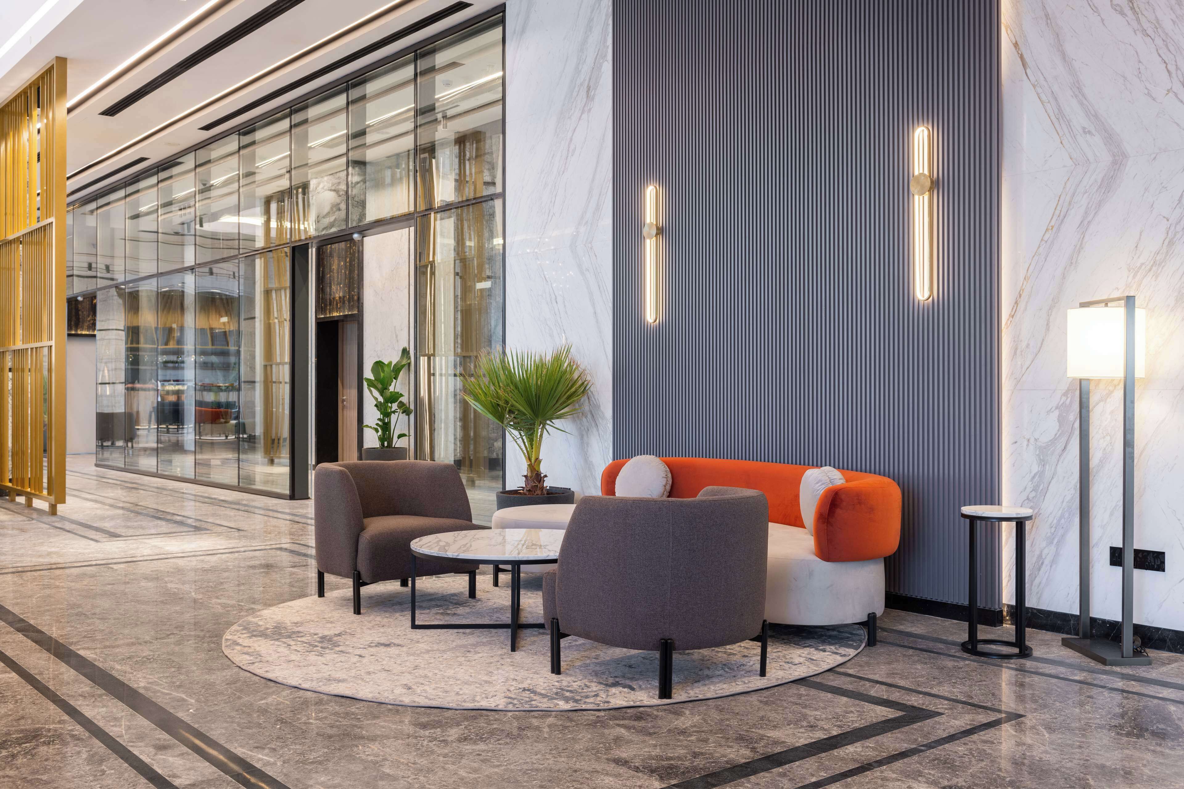 A modern lobby with a seating area featuring a sofa and armchairs, a small table, and a potted plant.