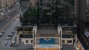 A modern high-rise building with a glass facade, a parking garage below, and a landscaped area in front. - Park Inn By Radisson Hotel & Apartments Kuwait (Mahboula)