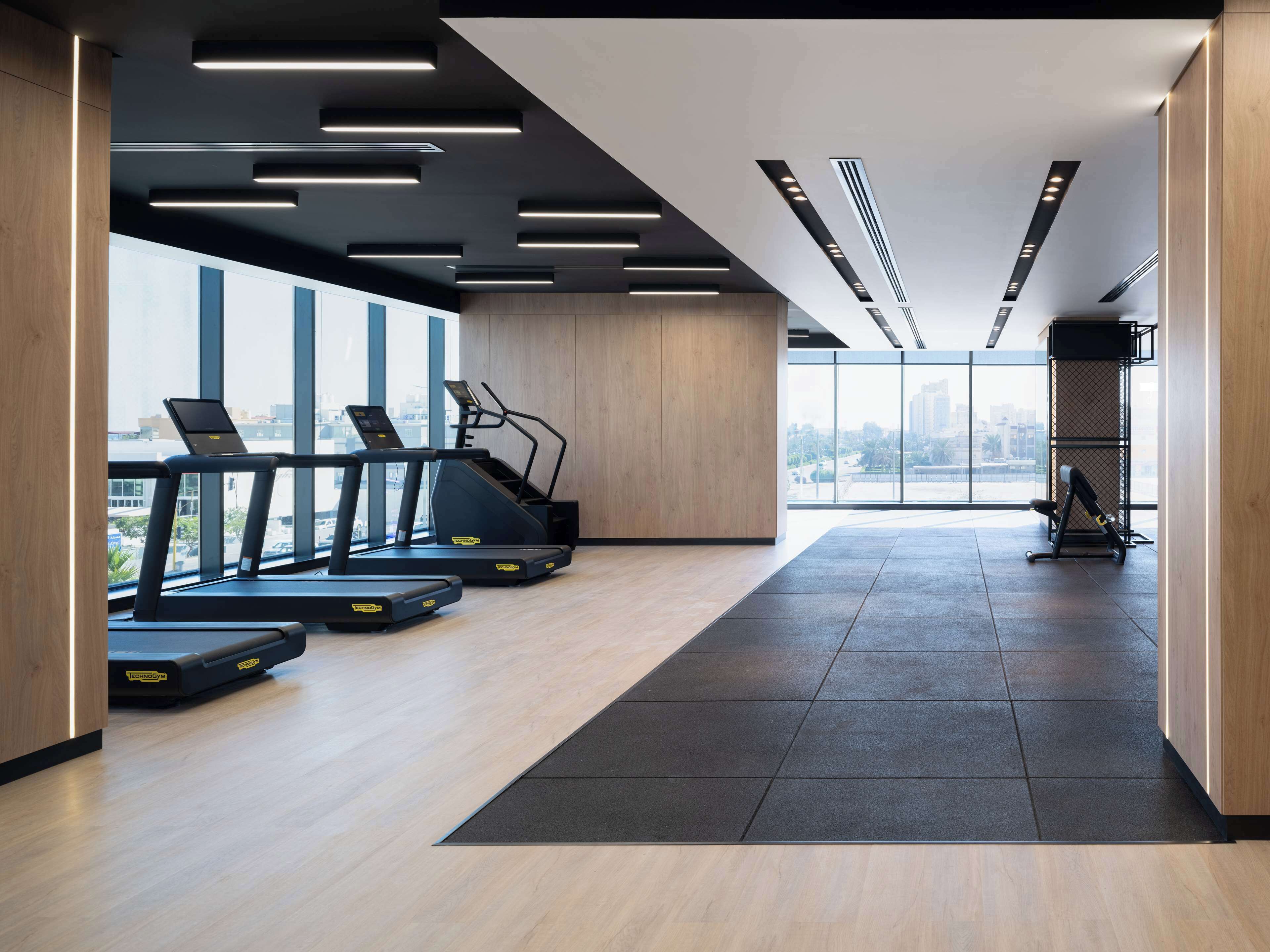 A modern gym with treadmills, a rowing machine, and a weight bench. Large windows offer a view of the city.