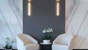 A modern lobby with marble walls, two white armchairs, a small table with a potted orchid, and vertical light fixtures. - Park Inn By Radisson Hotel & Apartments Kuwait (Mahboula)