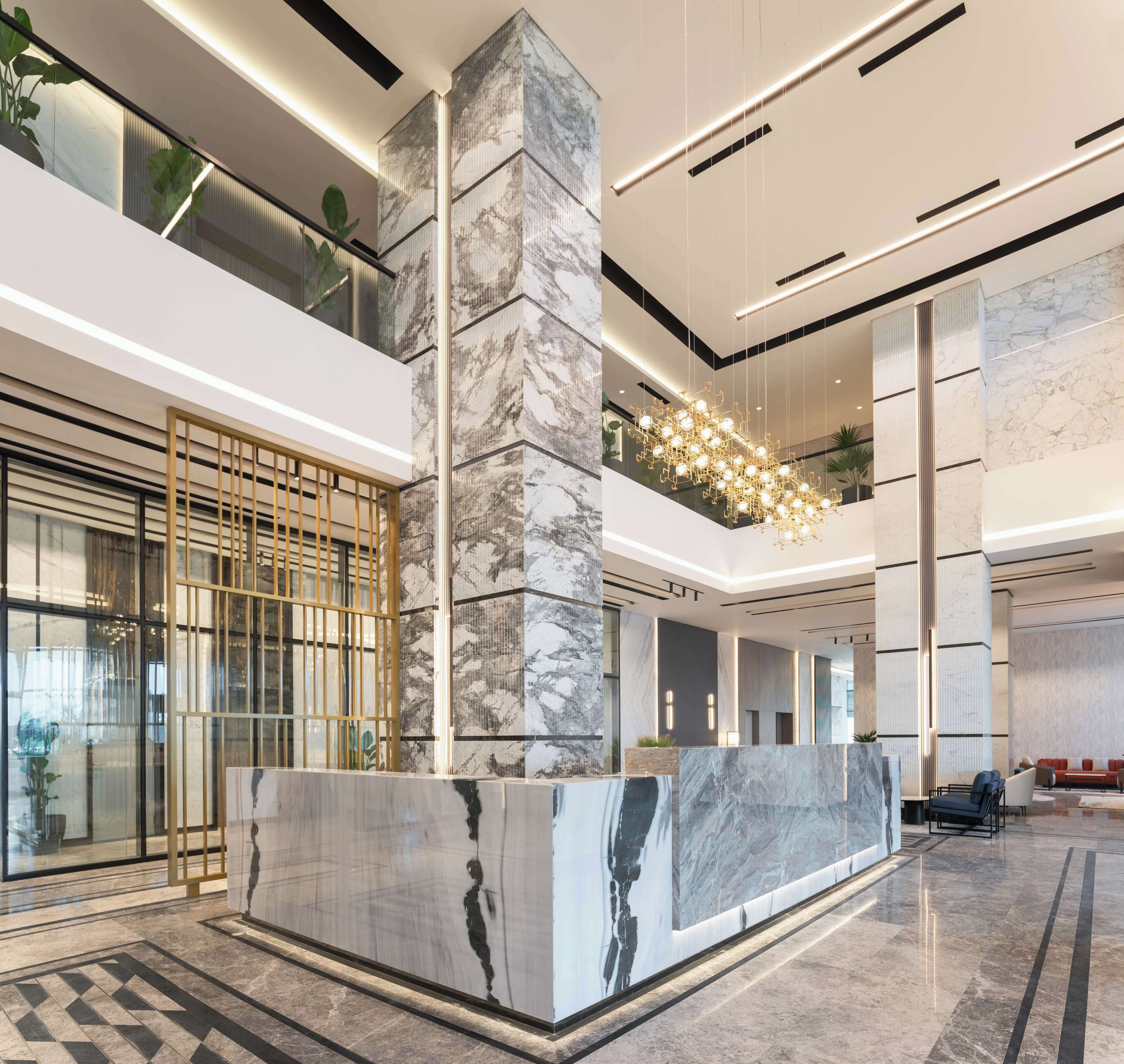 A spacious lobby with a marble reception desk, high ceilings, and modern lighting fixtures.