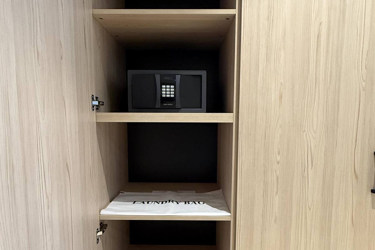 A wooden cabinet with a microwave on the top shelf, a laundry bag on the middle shelf, and a pair of shoes on the bottom shelf.