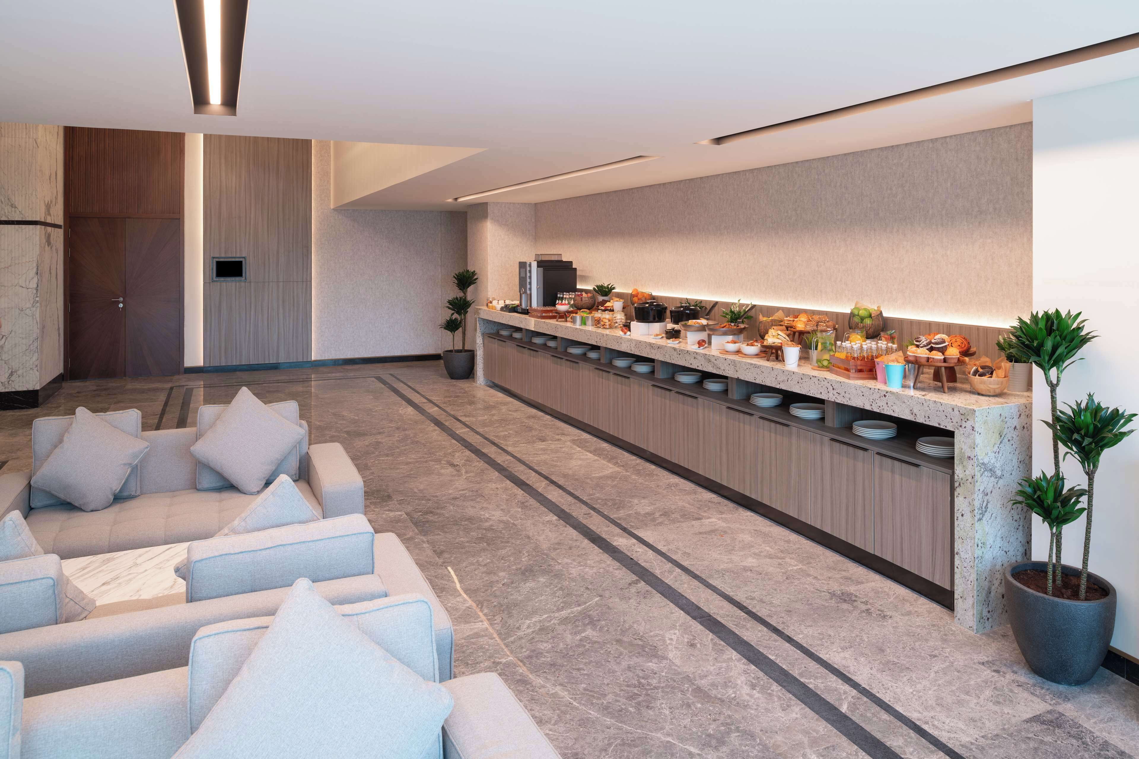 A modern hotel lobby with a long reception desk, seating area, and a large potted plant.