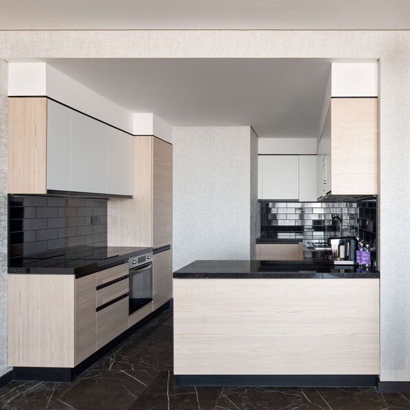 Una cocina moderna con armarios de madera clara, encimeras negras y salpicadero de azulejos negros.